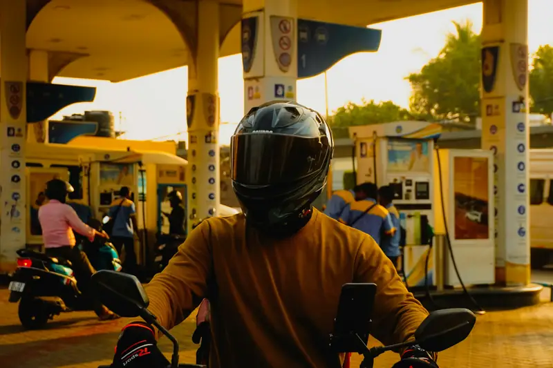 Motorista con casco repostando en una gasolinera al atardecer